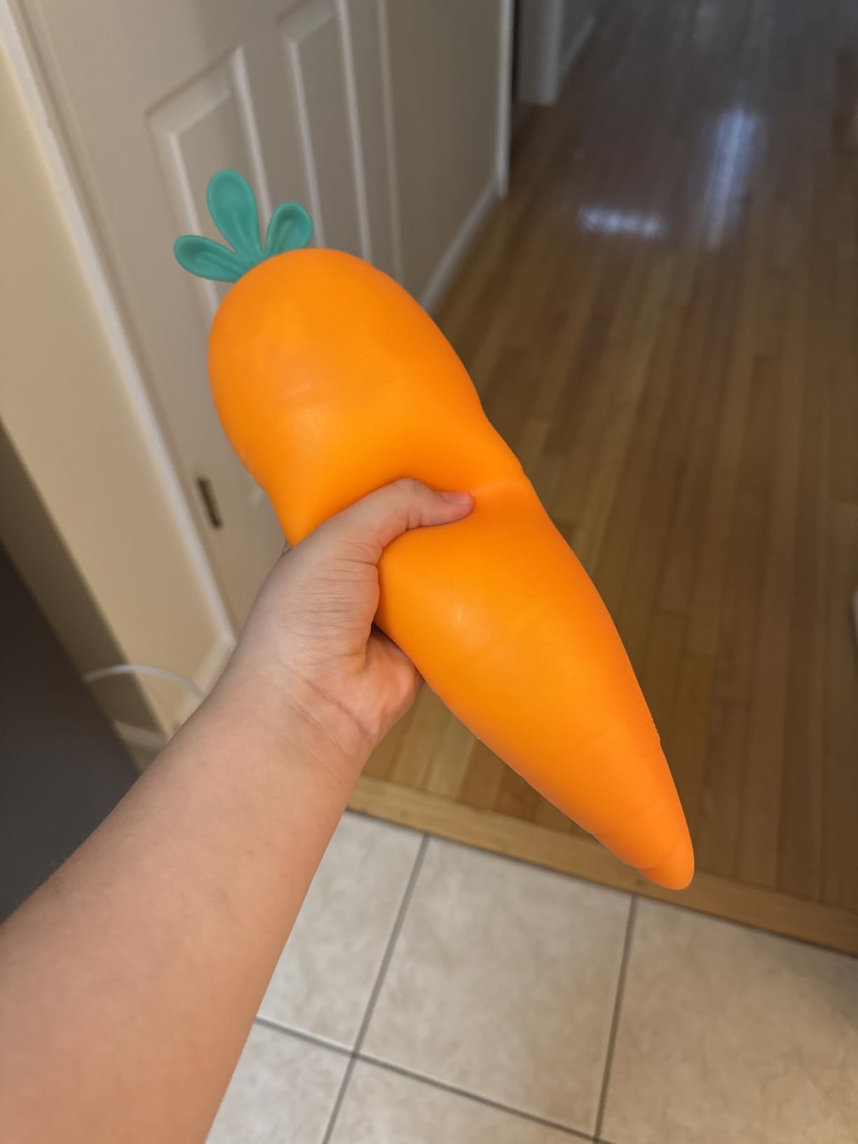 A hand squeezing the middle of the Toymendous Squishy Carrot, the material bunching up around the fingers
