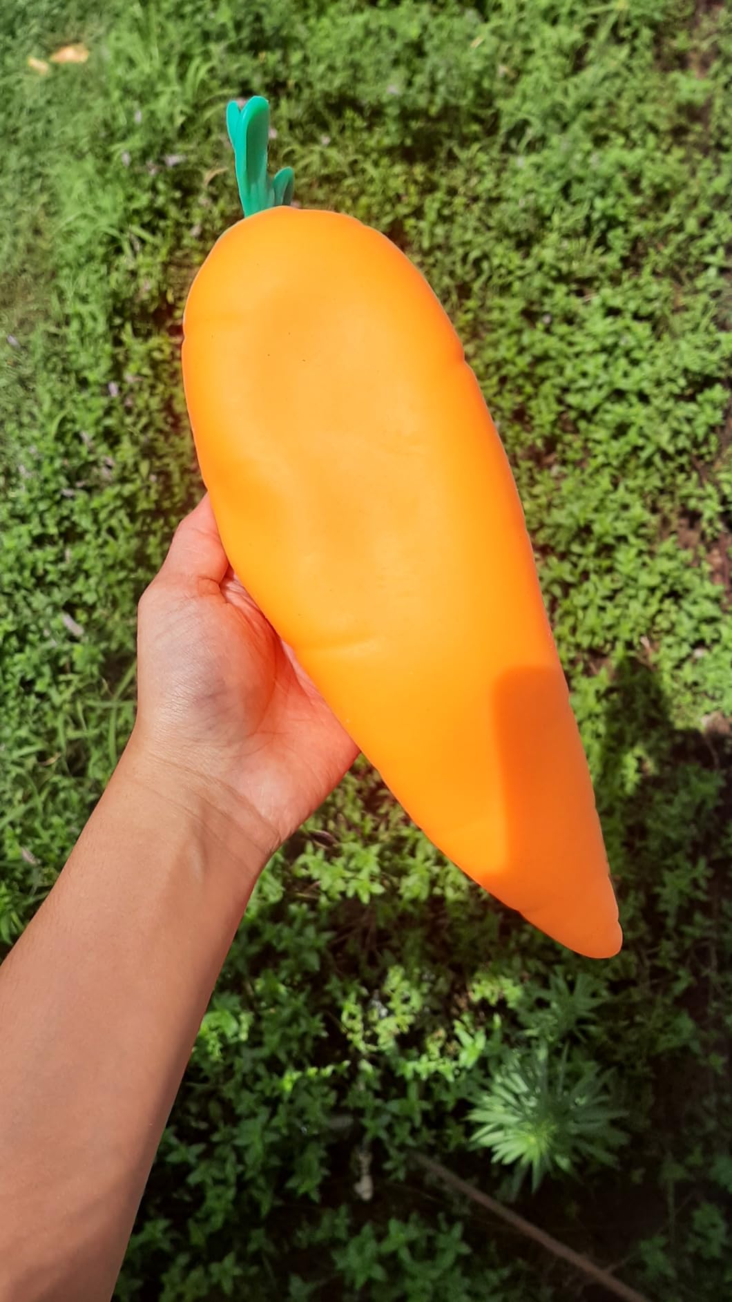 The Toymendous Squishy Carrot held up against grass, showing its full length from the teal top to the tapered tip