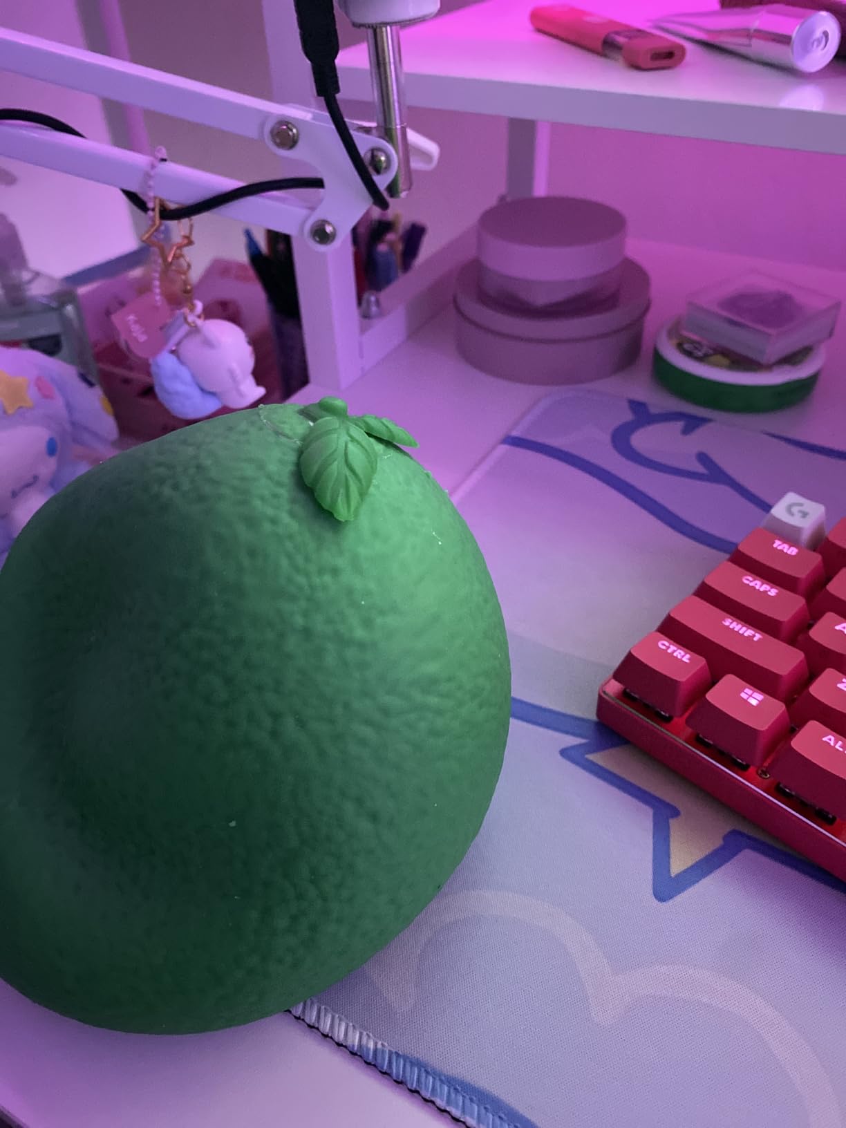The Toymendous Jumbo Squishy Lime on a desk mat beside a red mechanical keyboard under pink lighting