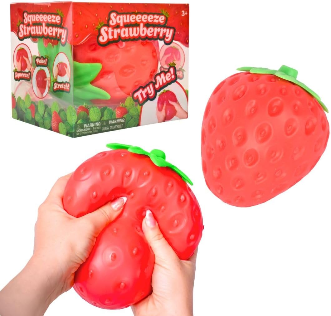 Sunny Days Squeeze Strawberry, a red squishy strawberry with dimpled seed texture and a green leaf top, being flattened between two hands beside its box